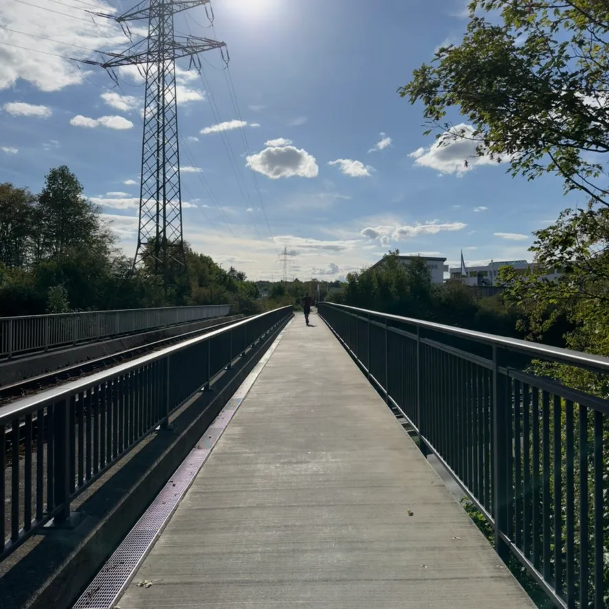 Footbridge under a sunny sky with a power pylon