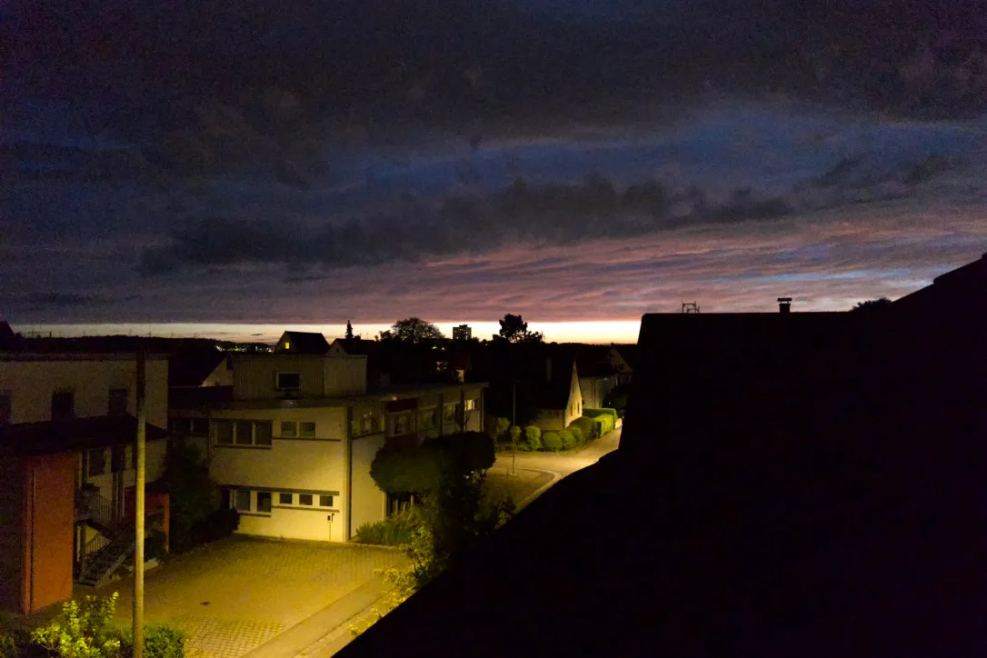 Rooftops under a dark sky with the last light on the horizon